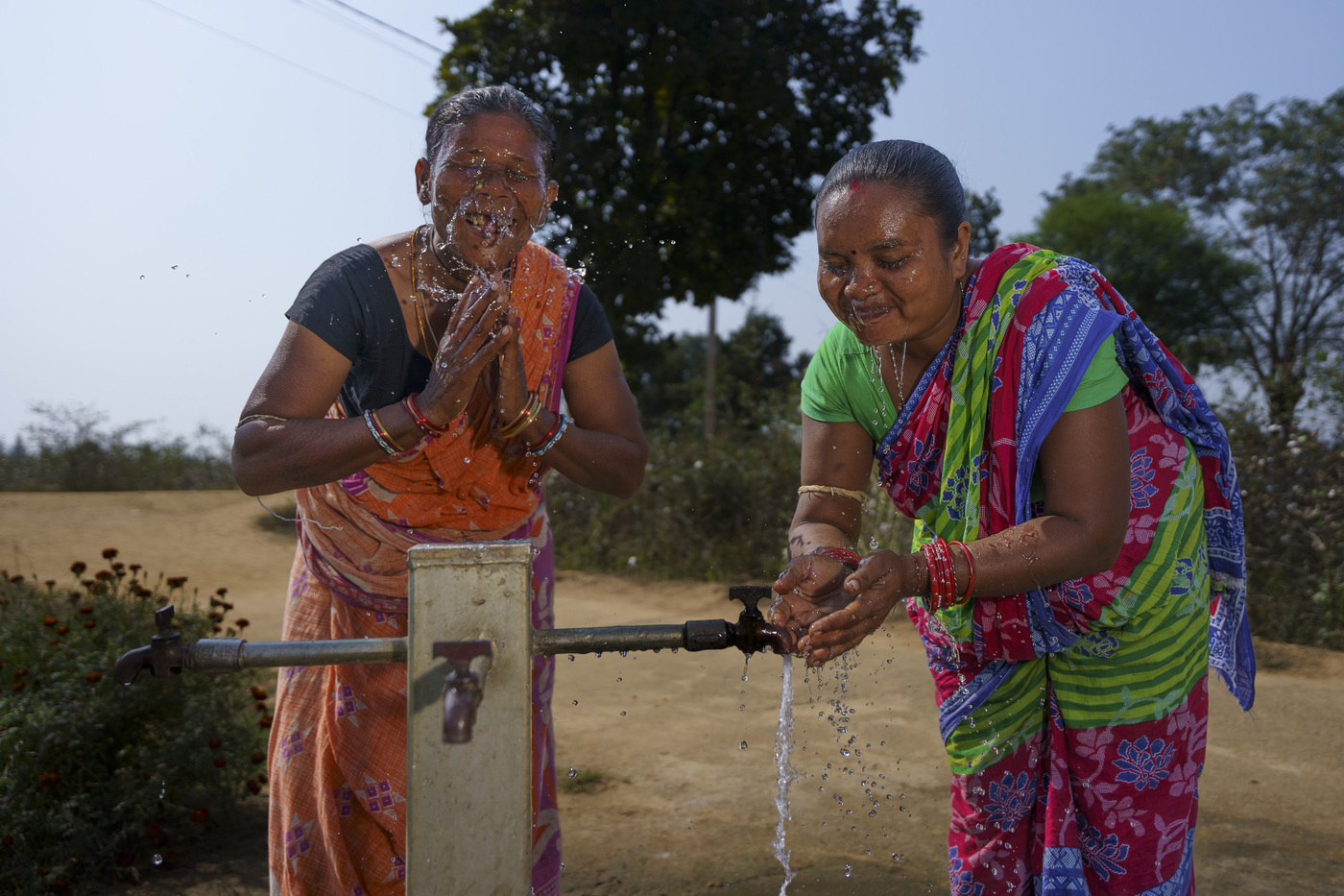 Zwei Baumwollbäuerinnen waschen sich am Brunnen das Gesicht. 