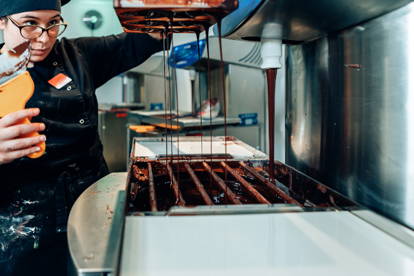 Chocolatier bei der Arbeit an einer Machine, die flüssige Schokolade ausgibt
