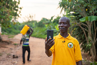 Ein Kakaobauer in gelbem T-Shirt filmt sich mit dem Smartphone.