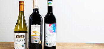 Drei Fairtrade-Weinflaschen stehen auf einem Holztisch.