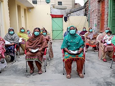 Frauen mit Mundschutz nehmen in einer pakistanischen Community an einem Workshop zur Aufklärung gegen das Coronavirus teil