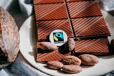 Foto: Schokolade und Kakaobohnen, darauf ein Button mit Fairtrade-Siegel