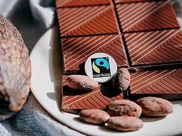 Fairtrade-Kakaoprodukte werden immer beliebter. Zu sehen: Symbolbild mit Schokotafel, Kakaobohnen und Schote mit Fairtrade-Siegel Foto: Ilkay Karakurt/Fairtrade