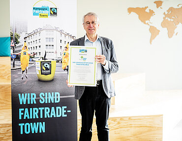 TransFair-Vorstandsvorsitzender Dieter Overath hält eine Urkunde in der Hand.