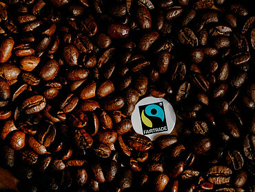 Ein Fairtrade-Siegel liegt inmitten gerösteter Kaffeebohnen.