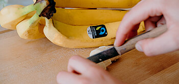 Eine Fairtrade-Banane wird auf einem Holzbrett in kleine Stücke geschnitten.
