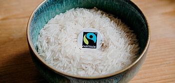 Reiskörner liegen in einer Schüssel, mittendrin liegt das Fairtrade-Siegel.