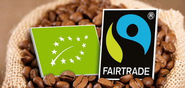 Ein Bio-Siegel liegt neben einem Fairtrade-Siegel in einem Sack Kaffeebohnen. 
