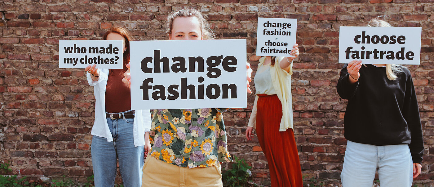 Vier Personen halten Schilder mit dem Slogan "Change Fashion" hoch.